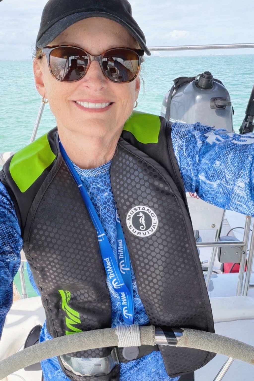 Woman on a sailboat wearing a sun protective shirt, shorts, sunglasses, and a life jacket